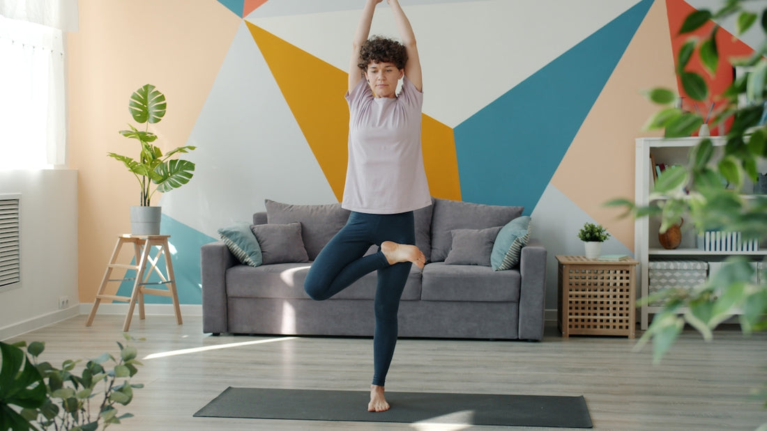 Woman practicing yoga tree pose in living room.