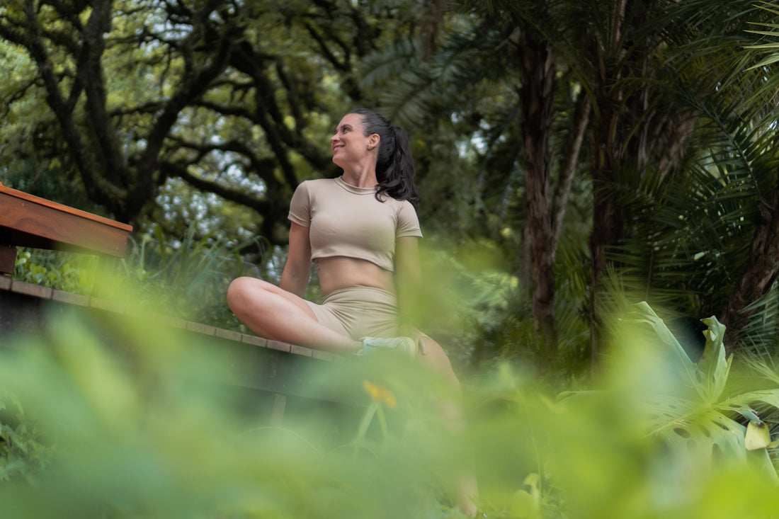 A woman meditating outdoors amidst lush greenery.