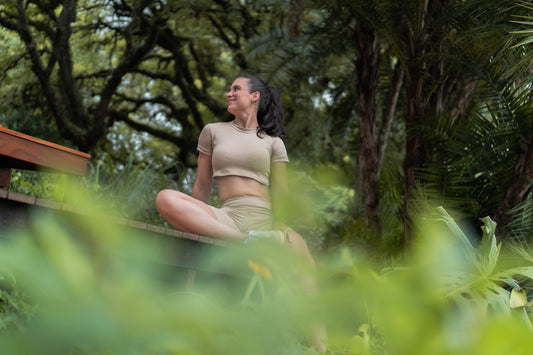 A woman meditating outdoors amidst lush greenery.
