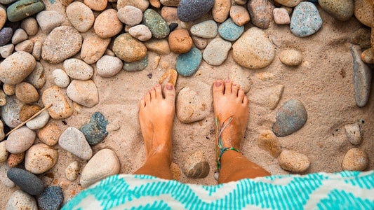 Feet standing on sand and pebbles at the beach.