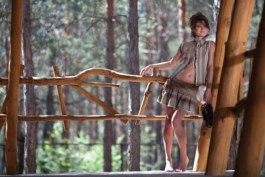 Barefoot woman stands on wooden balcony overlooking a forest.